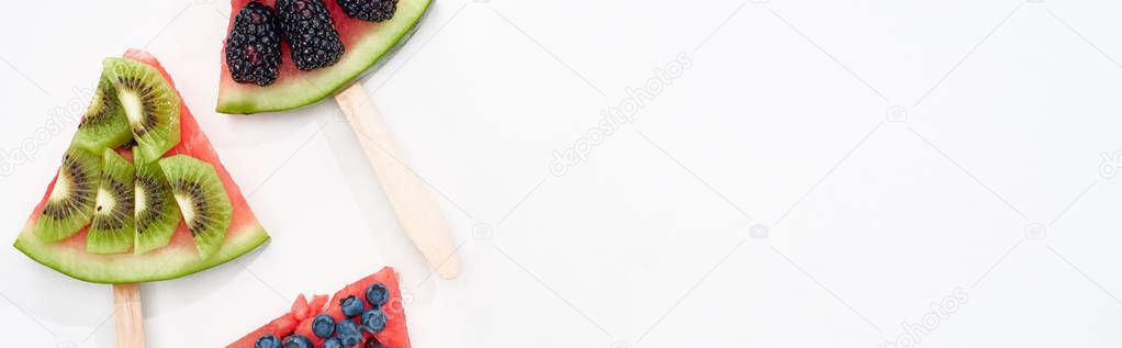 panoramic shot of delicious watermelon on sticks with seasonal berries and kiwi on white background
