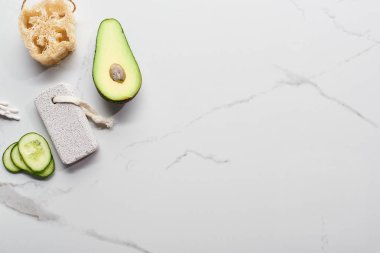 loofah, kulak çubukları ve mermer yüzeyde pomza taşı yakınında taze avokado ve salatalık üst görünümü
