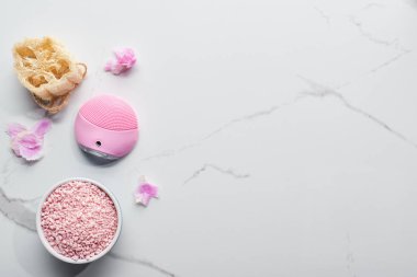 silikon temizleyici yüz fırçası üst görünümü, banyo tuzları ve pembe yaprakları ile mermer yüzeyinde loofah 
