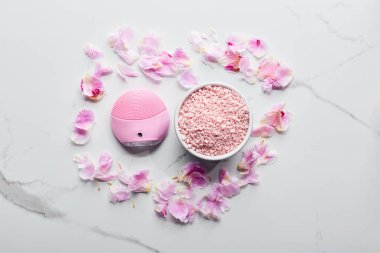 pembe yaprakları ile mermer yüzeyinde silikon temizlik yüz fırçası ve banyo tuzları üst görünümü 