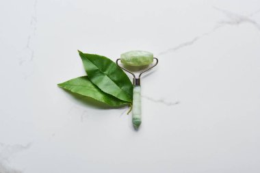 top view of jadeite facial roller and leaves on marble surface clipart