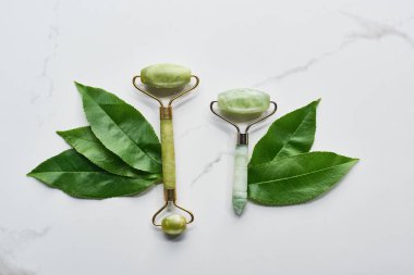top view of green facial rollers and leaves on marble surface clipart