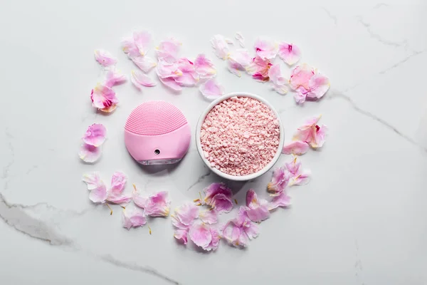 硅胶清洁面部刷子和浴盐在大理石表面与粉红色花瓣的顶视图 — 图库照片