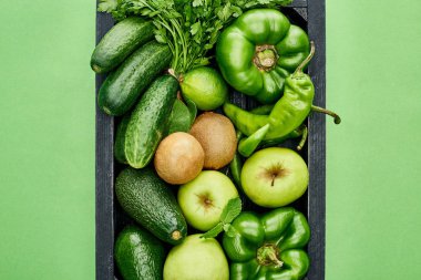 top view of apples, avocados, cucumbers, peppers, kiwi, greenery and zucchini in wooden box clipart