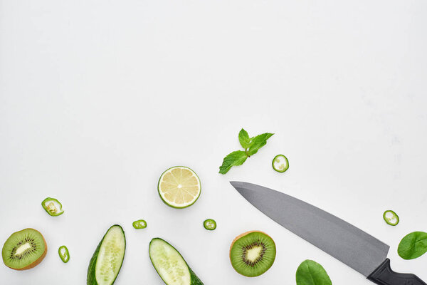  top view of knife, fresh cucumbers, kiwi, lime, peppers and greenery 
