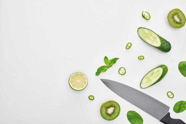  top view of knife, fresh cucumbers, kiwi, lime, peppers and greenery 