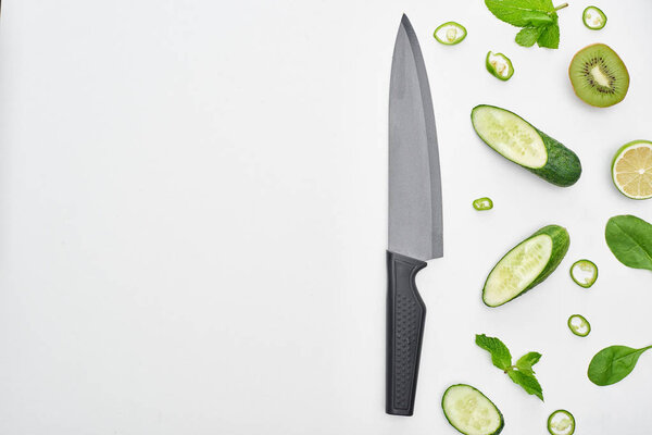  top view of knife, fresh cucumbers, kiwi, lime, peppers and greenery 