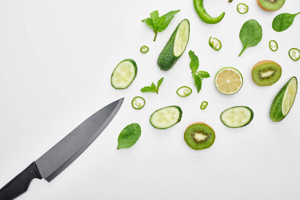 top view of knife, fresh cucumbers, kiwi, lime, peppers and greenery 