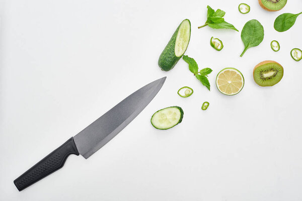  top view of knife, fresh cucumbers, kiwi, lime, peppers and greenery 