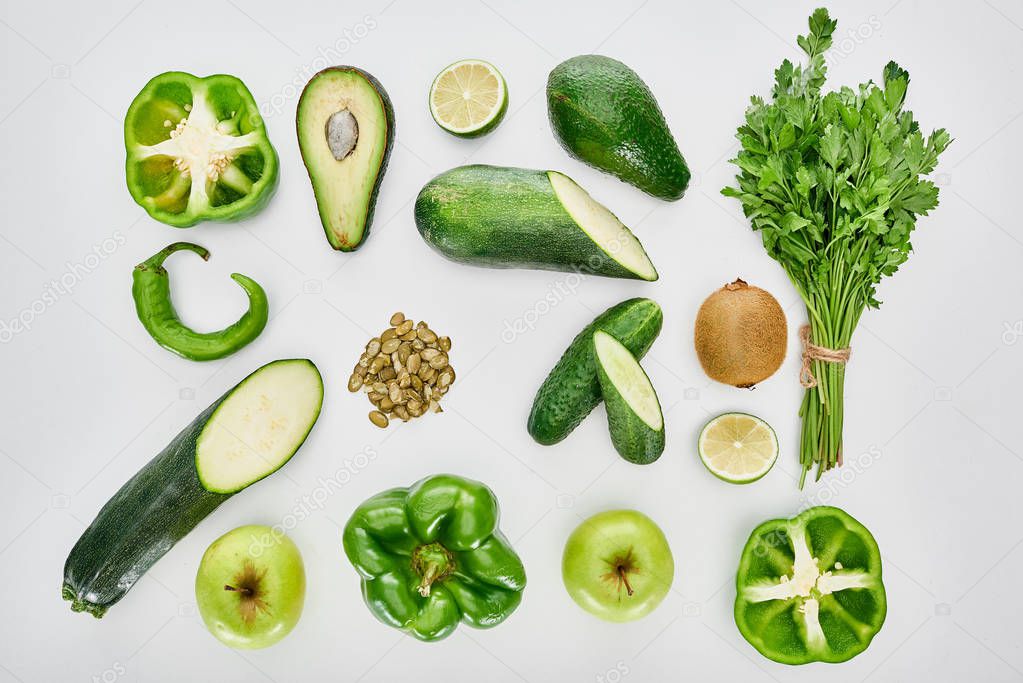 top view of apples, avocados, cucumbers, limes, peppers, kiwi, pumpkin seeds, greenery and zucchini