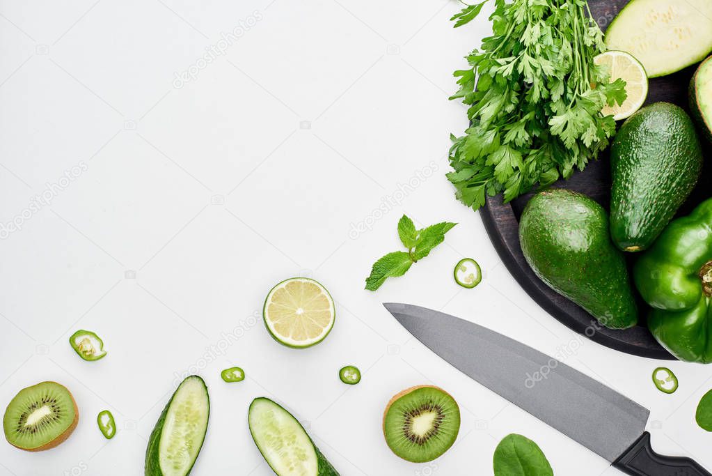 top view of knife, avocados, peppers, kiwi, limes and greenery on pizza skillet 