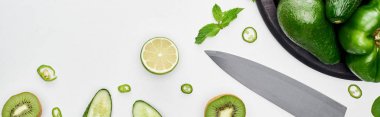 panoramic shot of knife, fresh cucumbers, kiwi, lime, peppers and greenery on pizza skillet clipart