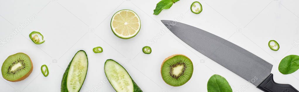  top view of knife, fresh cucumbers, kiwi, lime, peppers and greenery 