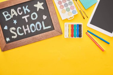Sarı arka plan üzerinde okul malzemeleri ve dijital tablet yakın okul yazıt geri ile ahşap çerçeve içinde Chalkboard