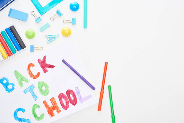 Top view of paper with back to school text near colorful felt-tip pens and school supplies isolated on white