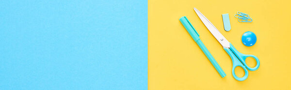 Panoramic shot of blue pen, scissors and paperclips on bicolor background