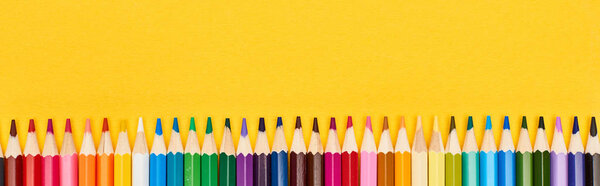 Панорамный снимок прямой линии цветных карандашей, изолированных на желтом
