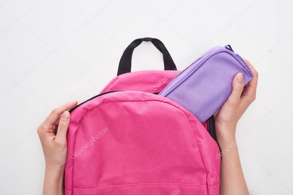 Partial view of schoolgirl taking violet pencil case from pink schoolbag isolated on white