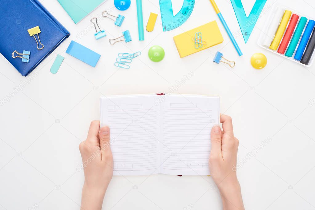 Top view of schoolgirl holding opened notebook with clear pages near stationery isolated on white