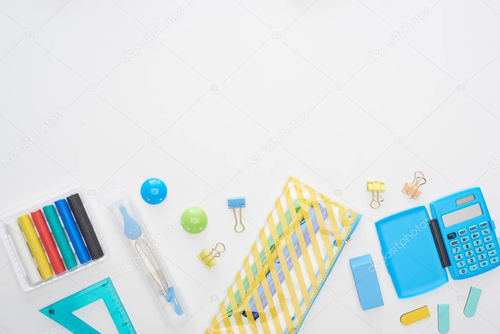 Top view of blue and yellow scattered school supplies with pencil case and calculator isolated on white