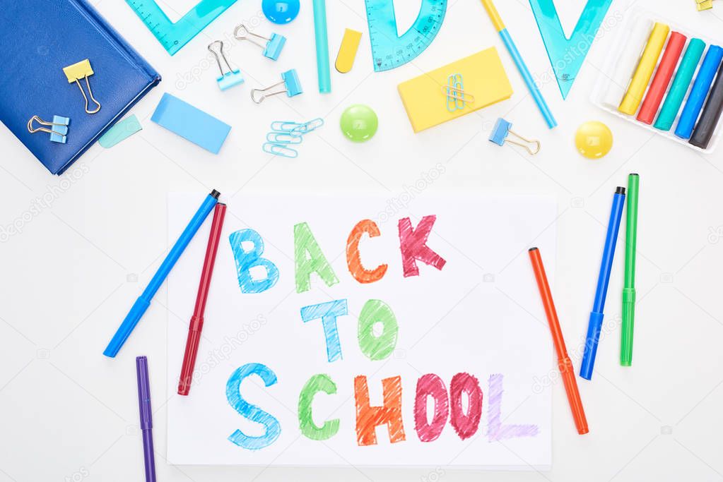 Top view of paper with back to school lettering near colorful felt-tip pens and stationery isolated on white