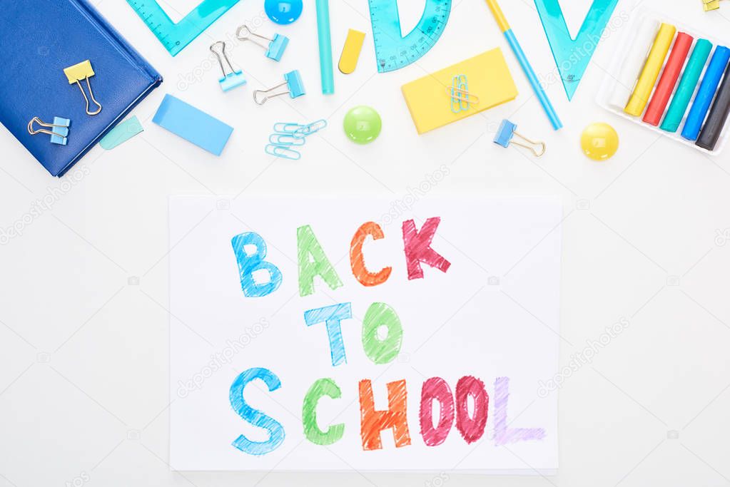 Top view of paper with back to school text near school supplies isolated on white