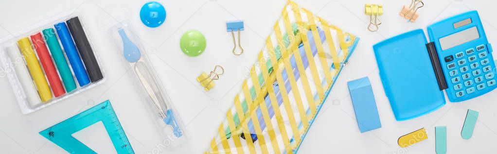 Panoramic shot of blue and yellow scattered school supplies with pencil case and calculator isolated on white