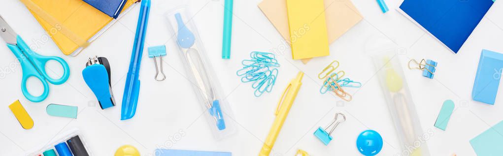 Panoramic shot of blue and yellow scattered school supplies with notepads isolated on white