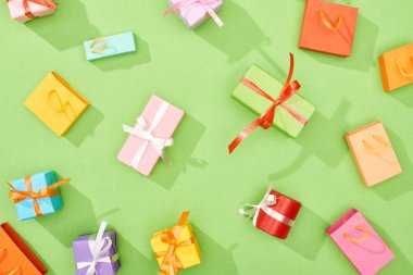 top view of scattered gift boxes and shopping bags on green background clipart