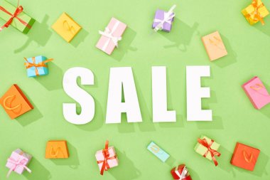 yeşil arka plan üzerinde satış yazı etrafında dağınık dekoratif hediye kutuları ve alışveriş çantaları üst görünümü