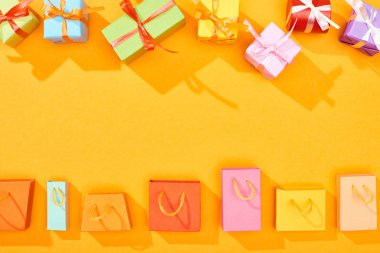 top view of festive wrapped gifts and shopping bags on bright orange background clipart
