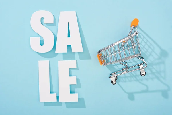 top view of white sale lettering and decorative shopping cart on blue background