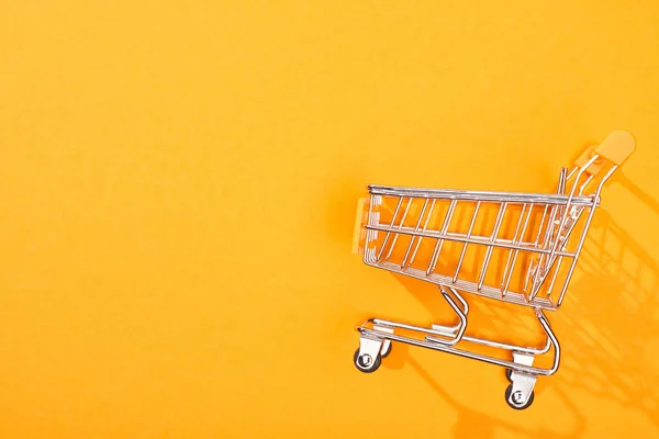 明るいオレンジ色の背景に空のショッピングカートのトップビュー — ストック写真