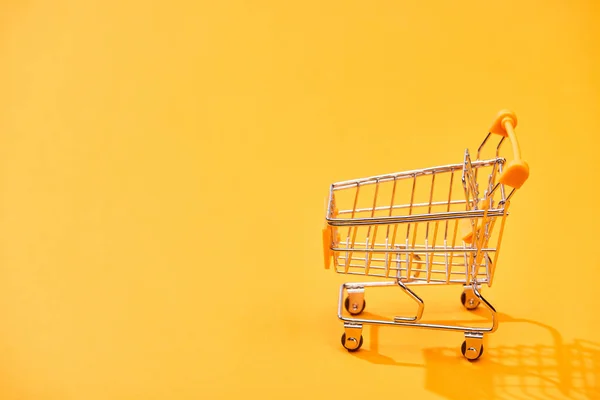 明るいオレンジ色の背景に空の装飾的なショッピングカート — ストック写真