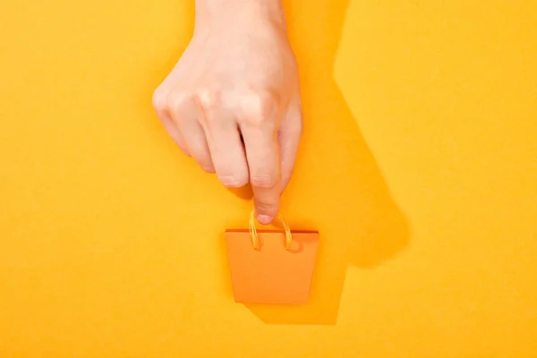 明るいオレンジ色の背景に小さなショッピングバッグを保持する手のトリミングビュー — ストック写真