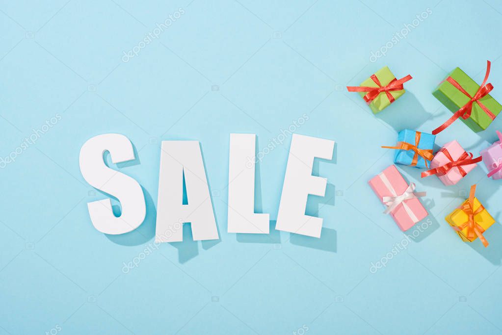 Top view of white sale lettering and festive gift boxes on blue background
