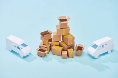 mavi arka plan üzerinde beyaz mini vanlar arasında karton kutular yığını