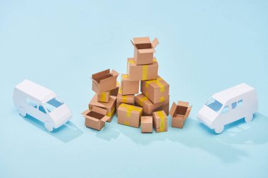 pile of cardboard boxes between white mini vans on blue background clipart