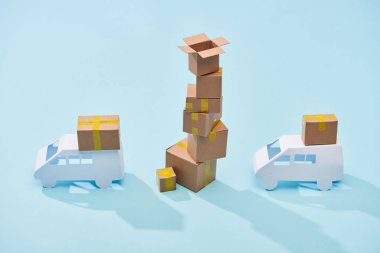 mavi arka plan üzerinde beyaz kamyonlar arasında karton kutular yığını