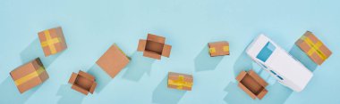 Panoramic shot of closed and open cardboard parcels near mini van on blue background clipart