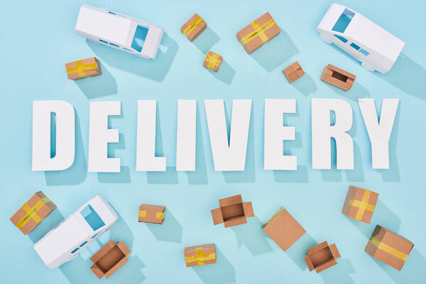 top view of delivery lettering with shadows near cardboard boxes and vans on blue background