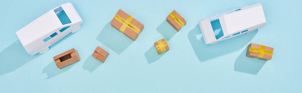 Panoramic shot of closed and open cardboard parcels near mini vans on blue background
