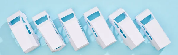 panoramic shot of miniature white autos on blue background