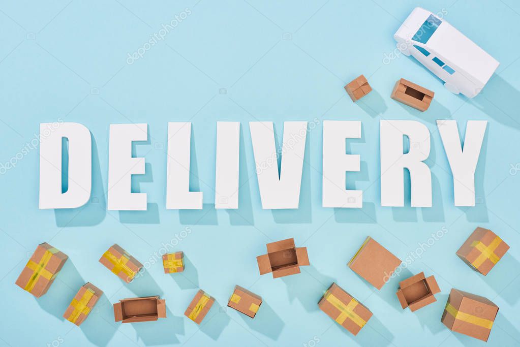 top view of delivery lettering with shadows near cardboard boxes and van on blue background