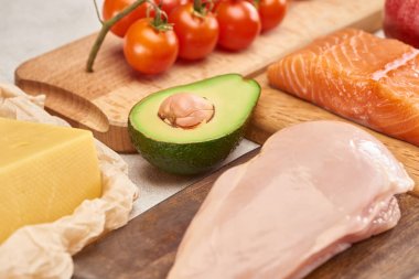 Taze çiğ kümes hayvanları, balık, peynir, kiraz domates dalı ve ahşap kesme tahtalarında avokado yarısı