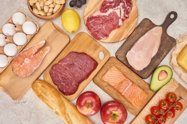 Üst görünüm af ham organik çeşitli et, kümes hayvanları, balık, yumurta, elma, limon, avokado, domates ve fıstık mermer yüzeyinde taze baget ile ahşap dolaplar üzerinde