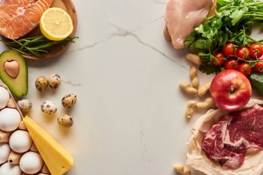 Çiğ et, kümes hayvanları ve yumurta, avokado, limon, peynir, domates, yer fıstığı ve yeşillik dalları dalı ile balık üst görünümü