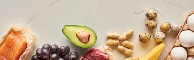 Avokado, yer fıstığı, bıldırcın ve tavuk yumurtası, peynir, üzüm, çiğ et ve balık yarısının mermer yüzeyinde fotokopi alanı ile panoramik çekim