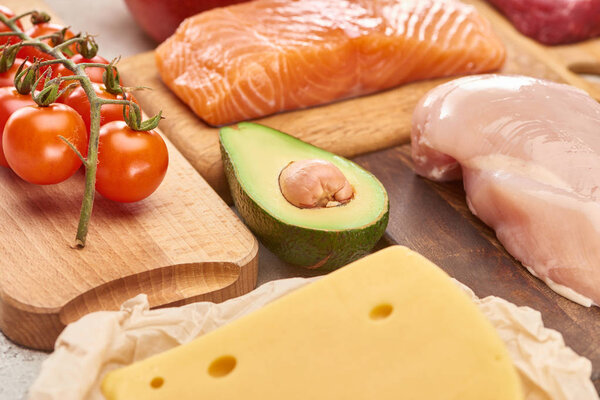 Свежая сырая рыба, птица, сыр, ветвь помидоров черри и половина авокадо на деревянных досках
