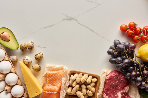 Top view of raw meat and fish with eggs, avocado, lemon, cheese, branch of tomatoes, grapes and peanuts